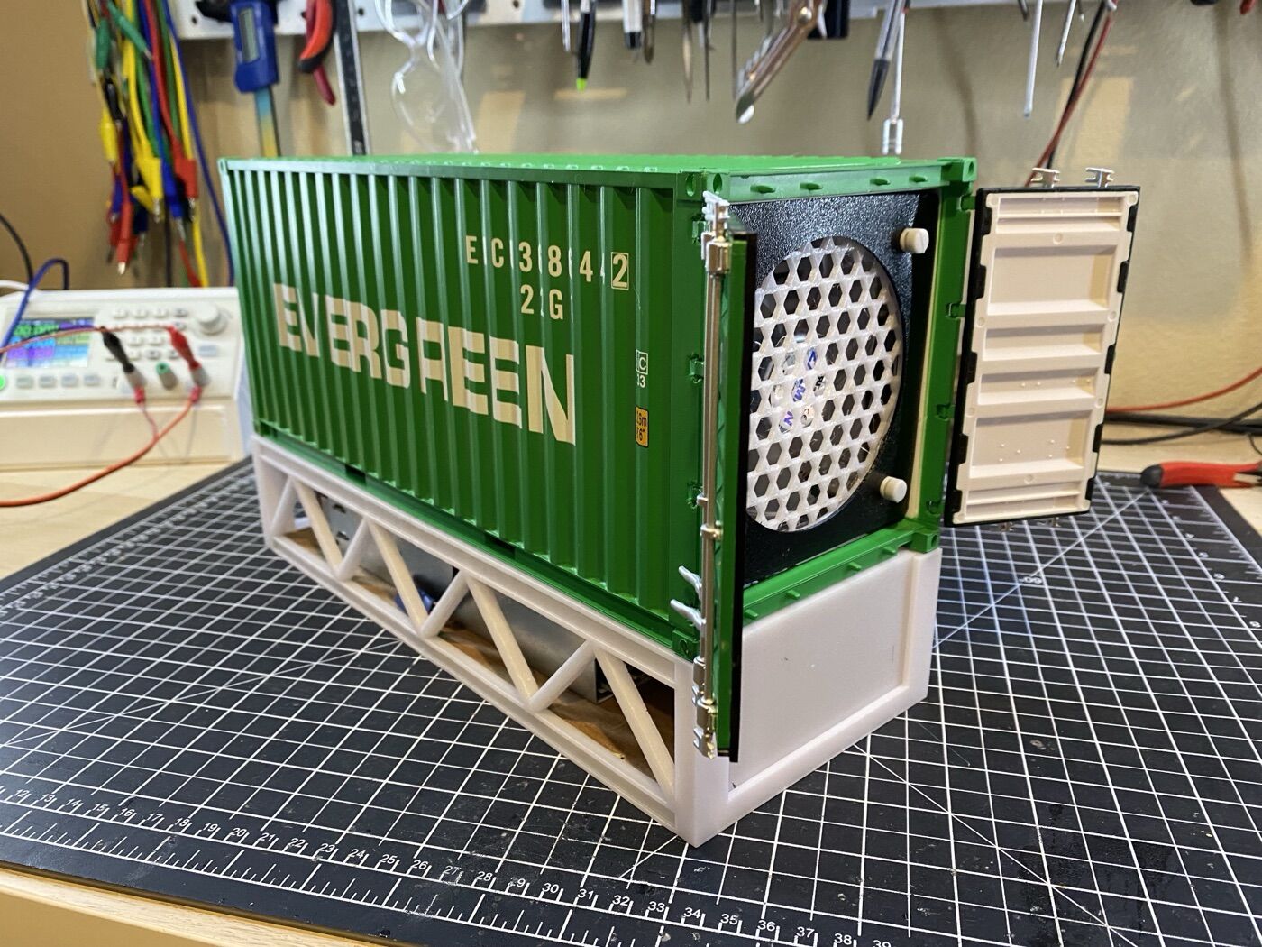 A green 1:20 scale Evergreen shipping container on a 3D-printed base, with its door open to show a cooling fan inside.
